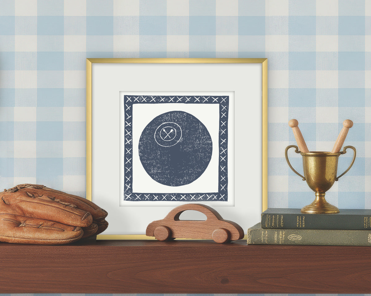 Framed artwork of a blue and white lacrosse ball on a white background, displayed on a shelf with a checkered wall.
