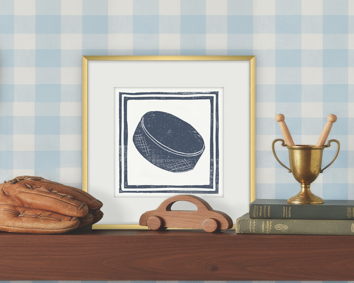 Framed artwork of a blue and white hockey puck on a white background, displayed on a shelf with a checkered wall.