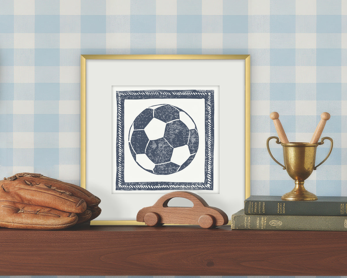 Framed artwork of a blue and white soccer ball on a white background, displayed on a shelf with a checkered wall.