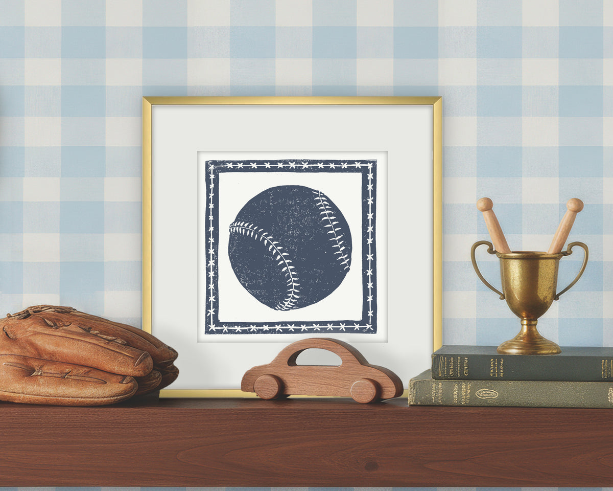 Framed artwork of a blue and white softball or baseball on a white background, displayed on a shelf with a checkered wall.