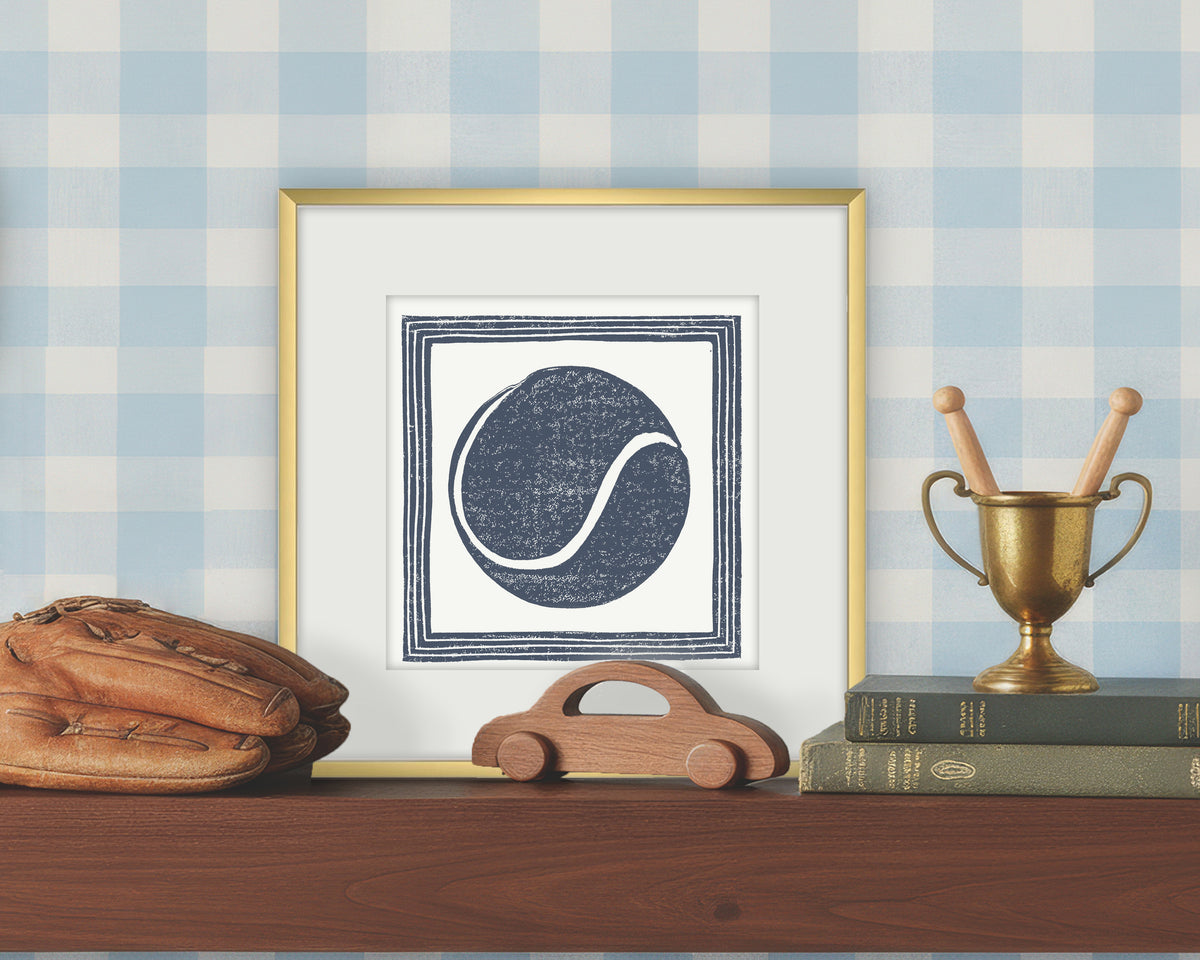 Framed artwork of a blue and white tennis on a white background, displayed on a shelf with a checkered wall.
