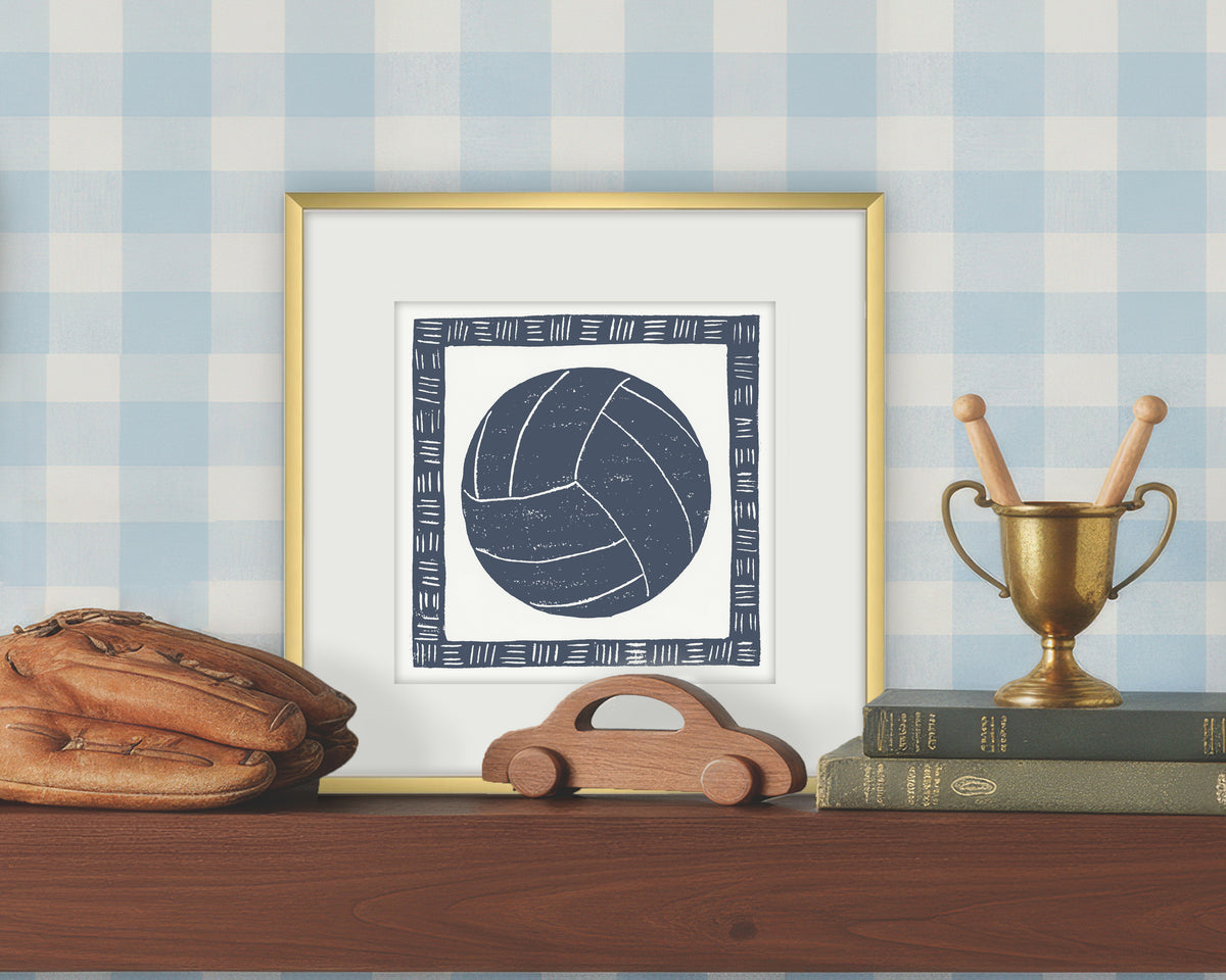 Framed artwork of a blue and white volleyball on a white background, displayed on a shelf with a checkered wall.