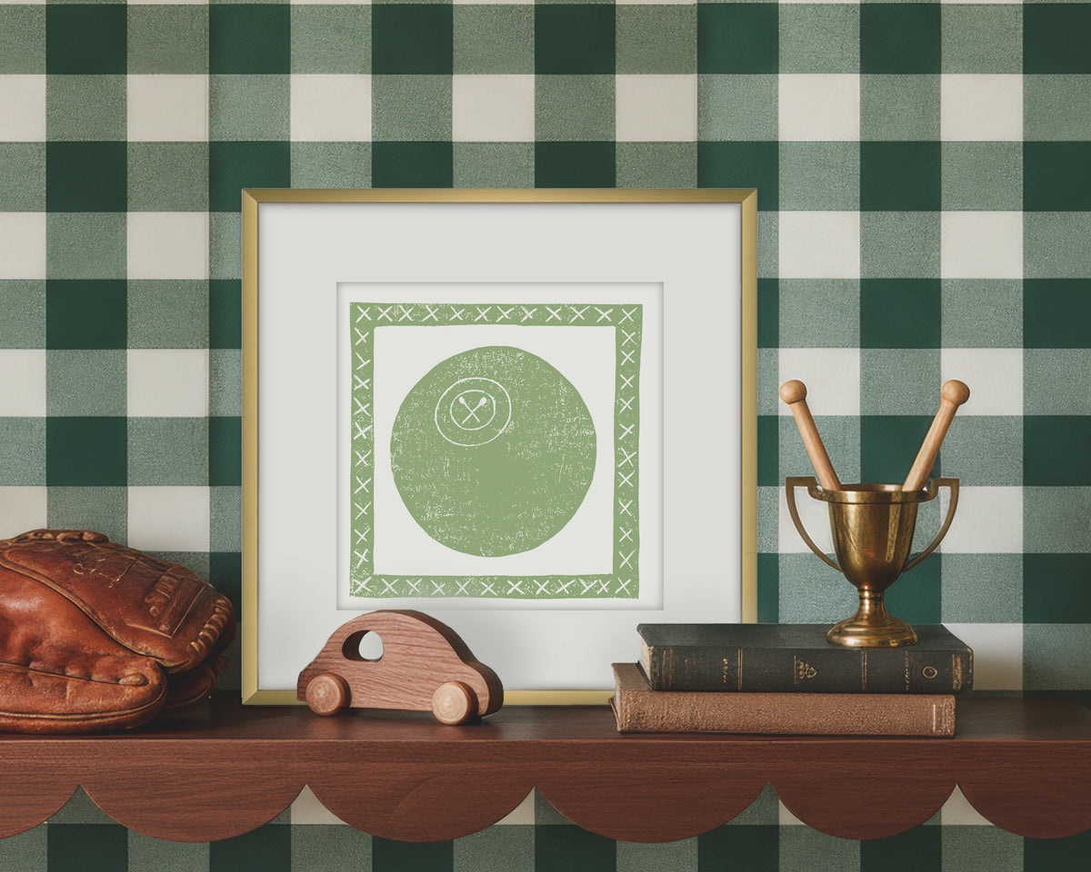 Framed artwork of a green and white lacrosse ball on a wooden shelf with decorative items against a green checkered wall.