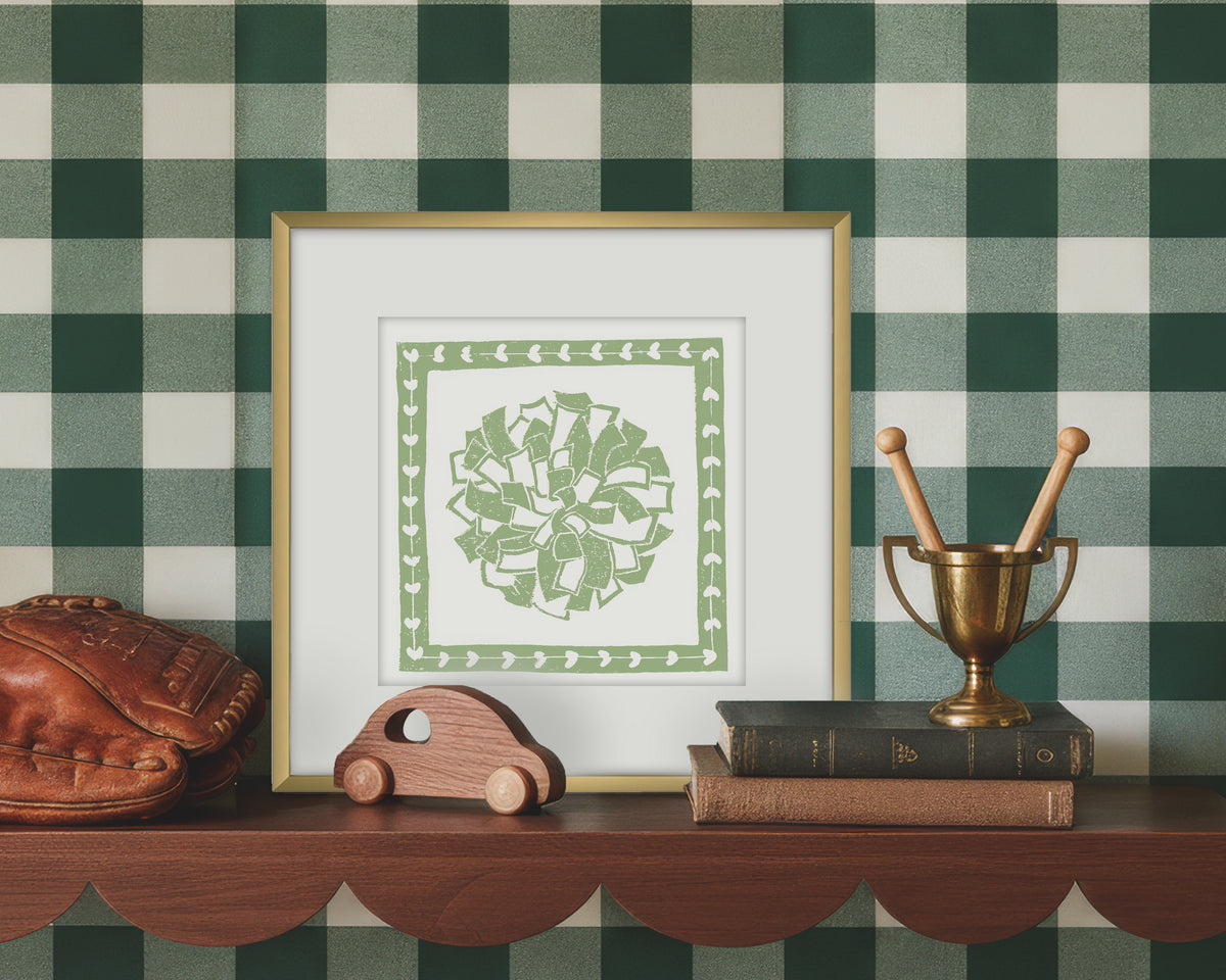 Framed artwork of a green and white cheerleading pom pon on a wooden shelf with decorative items against a green checkered wall.