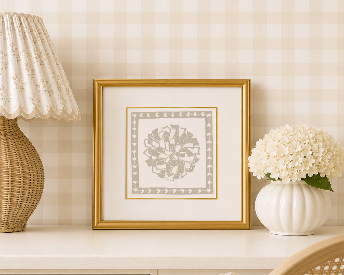 A sand tan and white pom pon art print in a gold matted frame on a styled shelf in a tan and white bedroom