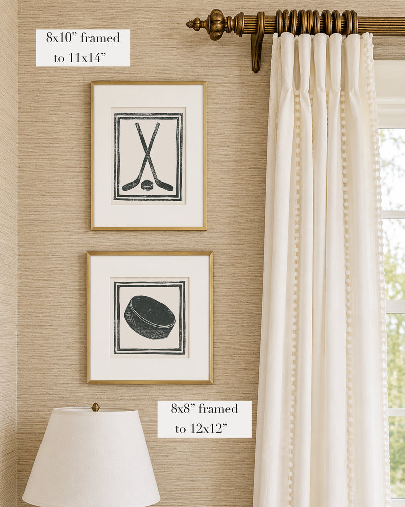 Framed black and white hockey themed artwork on a tan grasscloth wallpapered wall with a white window treatment and lampshade