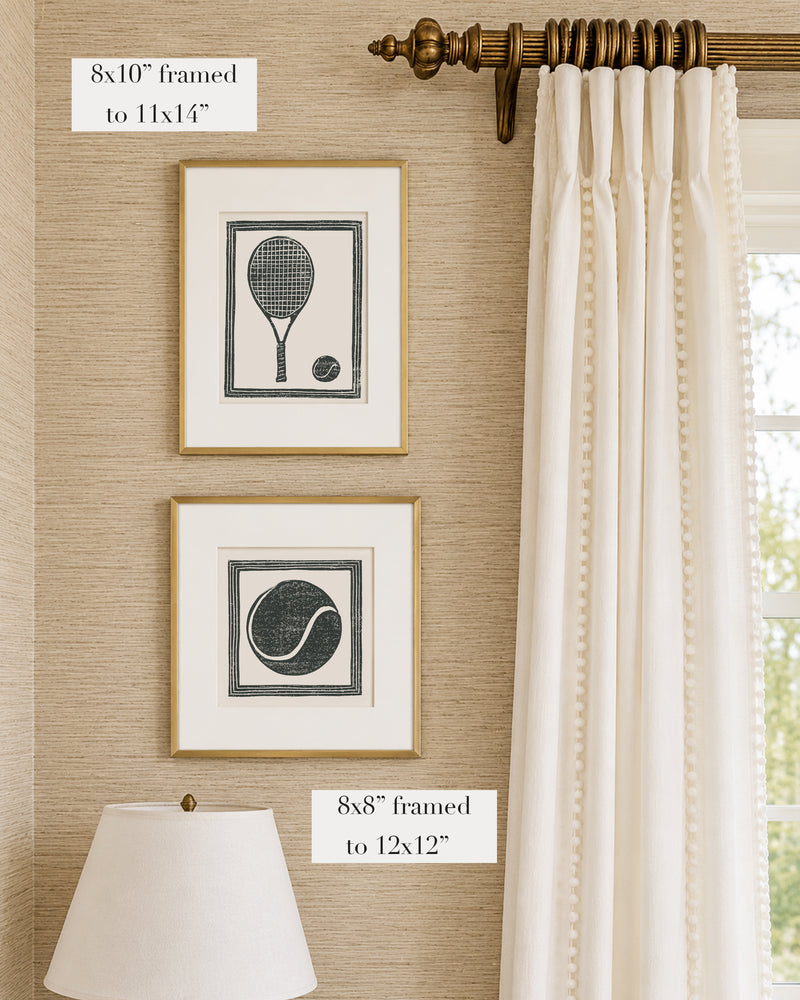 Framed black and white tennis themed artwork on a tan grasscloth wallpapered wall with a white window treatment and lampshade