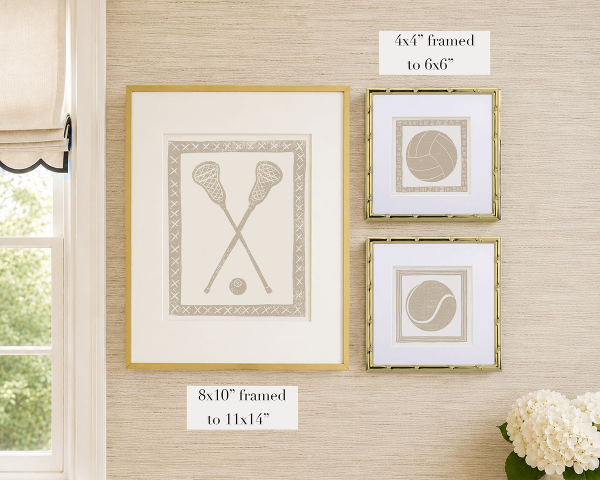 Framed tan and white sports themed artwork on a tan grasscloth wallpapered wall with window and floral decor.