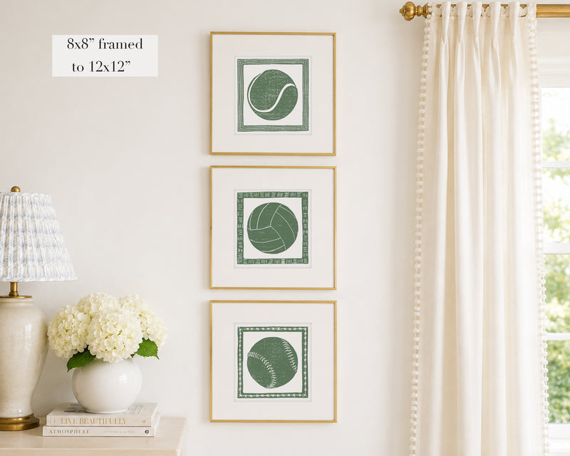 Trio of decorative grass green colored wall art with sports-themed prints on a white wall, next to a lamp and books.