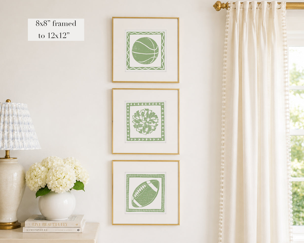 Trio of decorative sage green colored wall art with sports-themed prints on a white wall, next to a lamp and books.