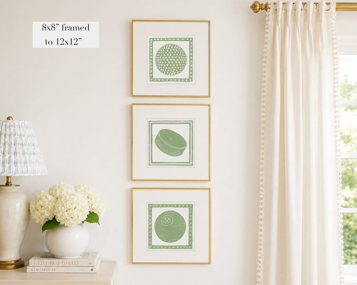 Trio of decorative sage green colored wall art with sports-themed prints on a white wall, next to a lamp and books.