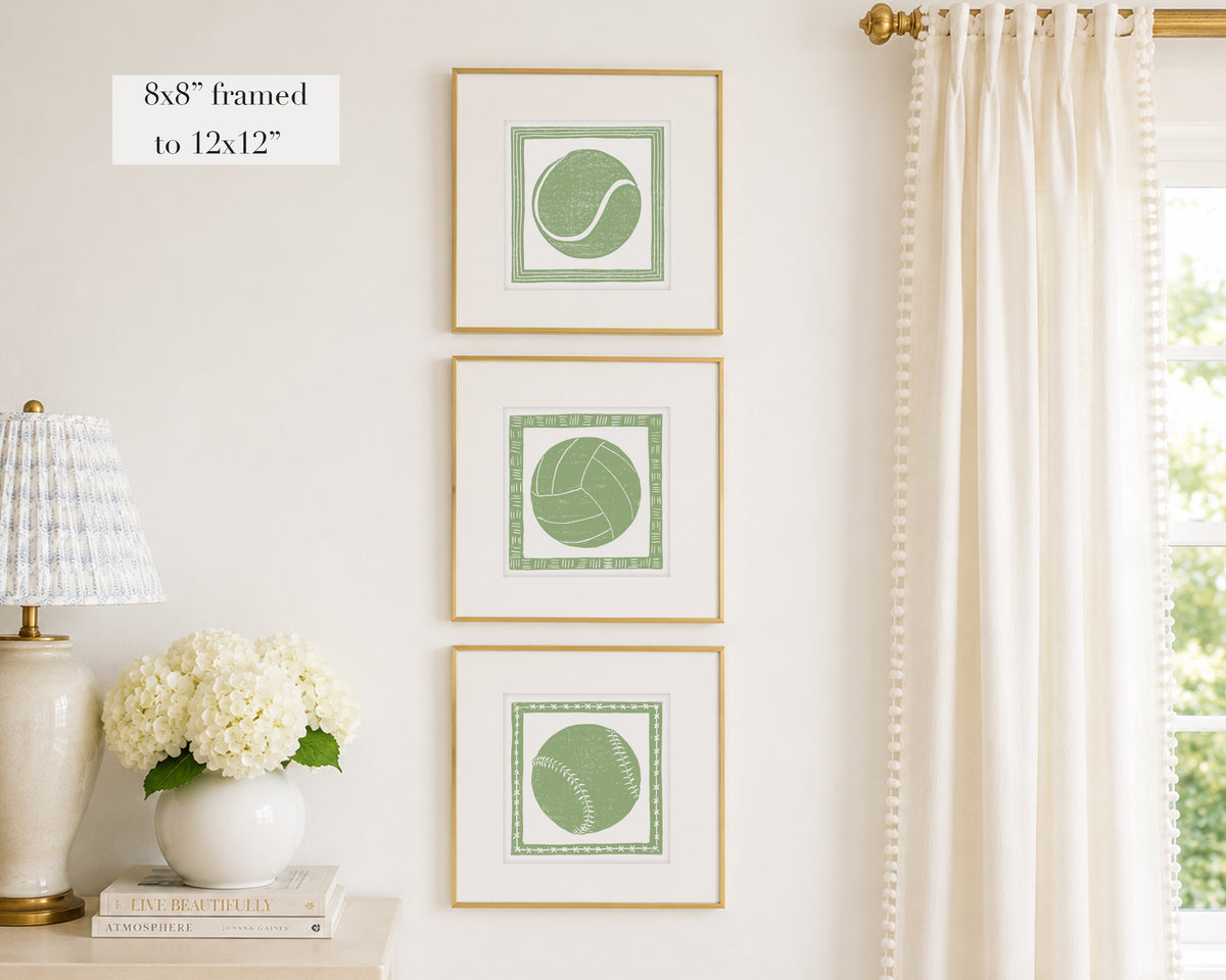 Trio of decorative sage green colored wall art with sports-themed prints on a white wall, next to a lamp and books.