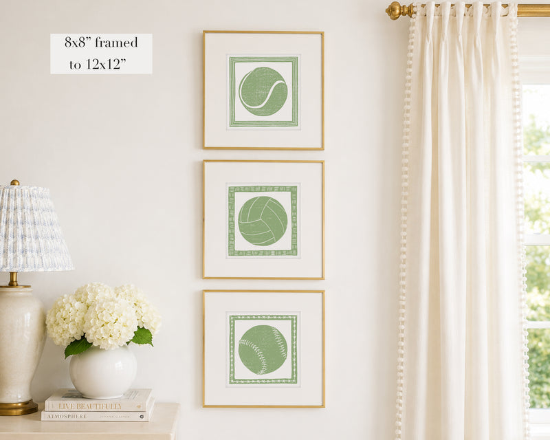 Trio of decorative sage green colored wall art with sports-themed prints on a white wall, next to a lamp and books.