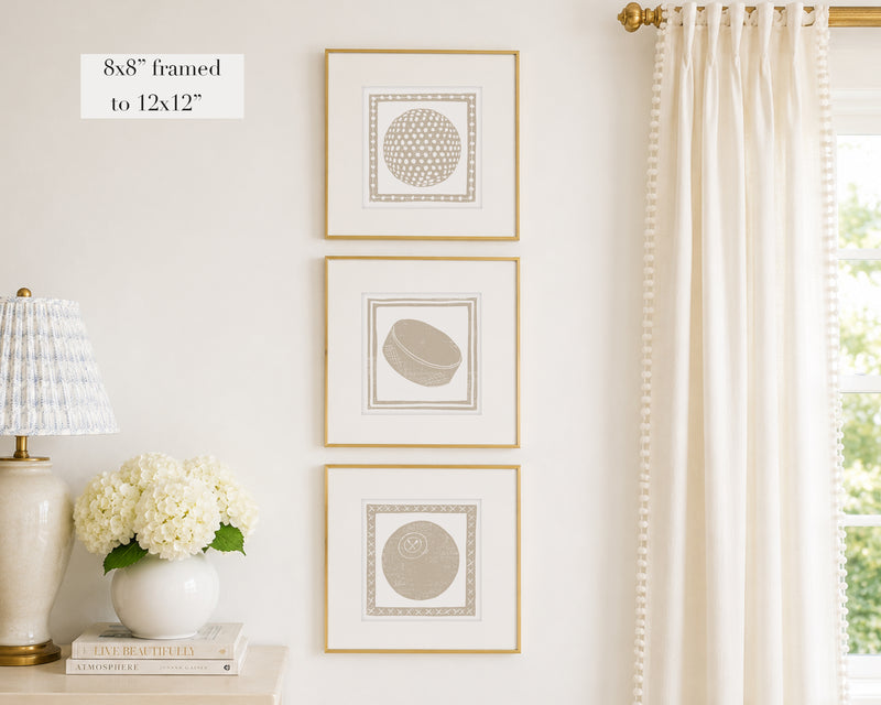 Trio of decorative tan colored wall art with sports-themed prints on a white wall, next to a lamp and books.
