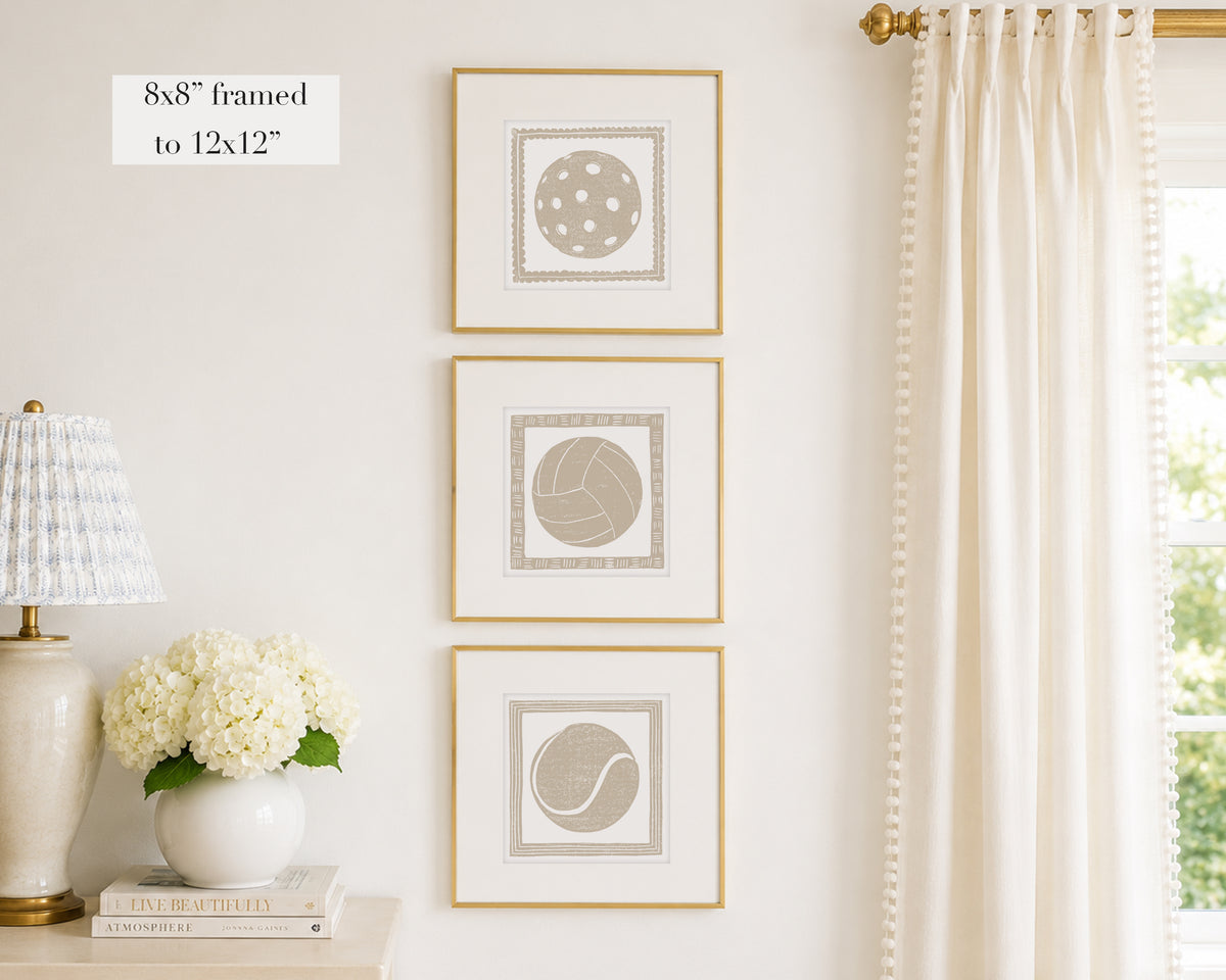 Trio of decorative tan colored wall art with sports-themed prints on a white wall, next to a lamp and books.