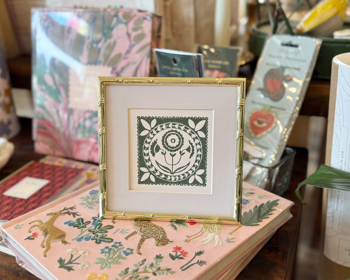 Framed artwork with a green design on a table with patterned books and stationery items.