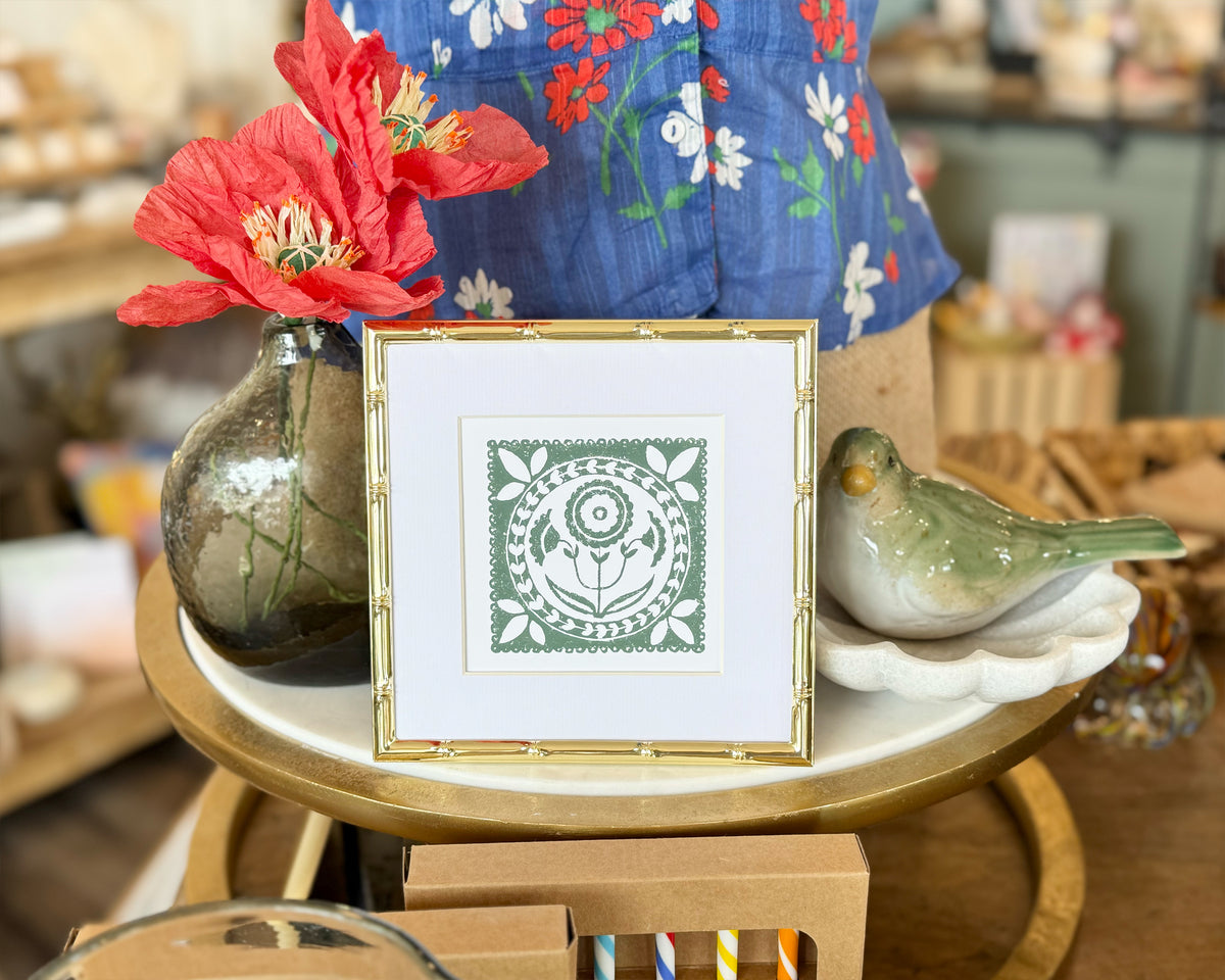 Decorative table with a framed green and white design, red flower, and ceramic bird.