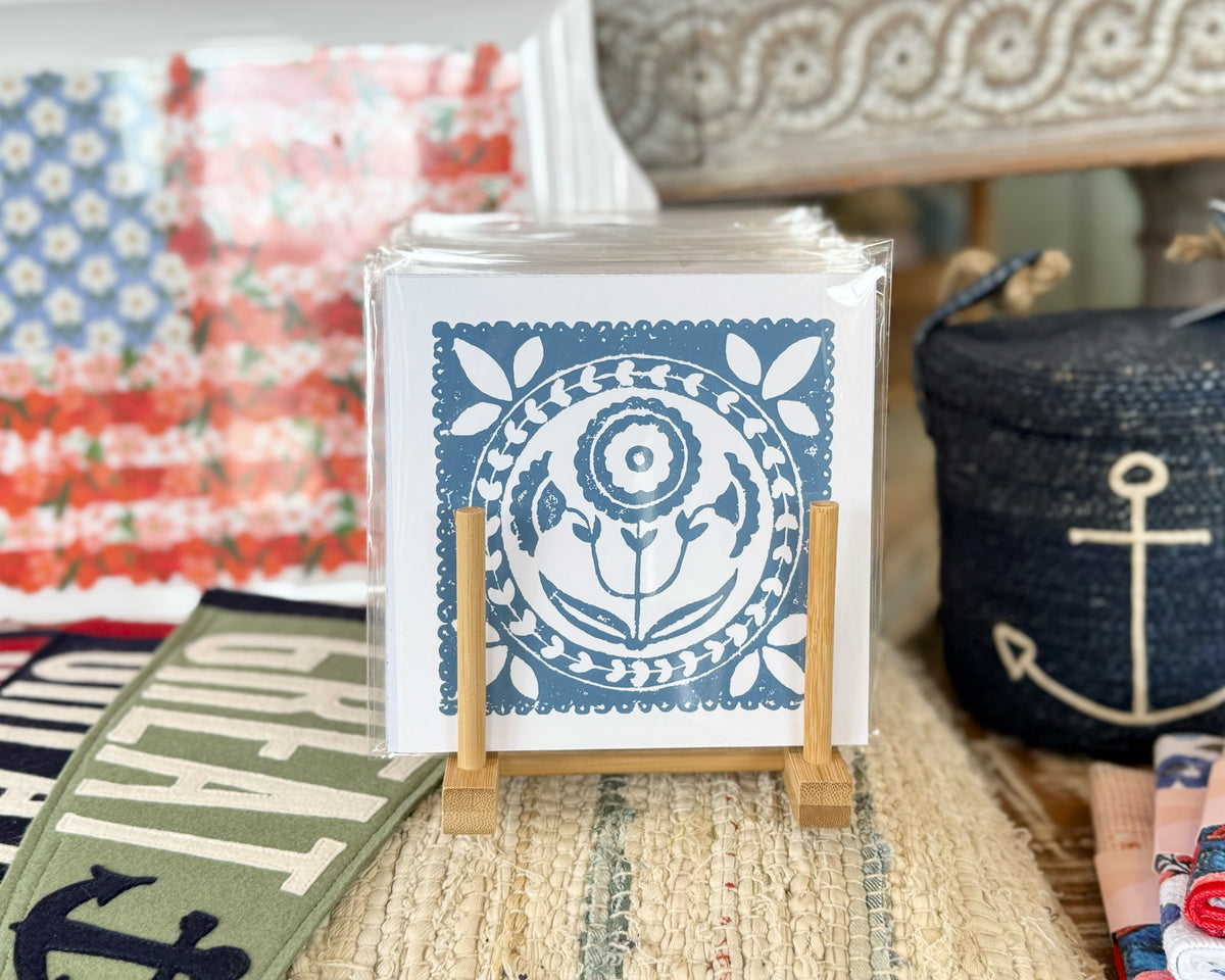 Decorative print with a blue floral design on a stand, surrounded by colorful fabric and a woven basket.
