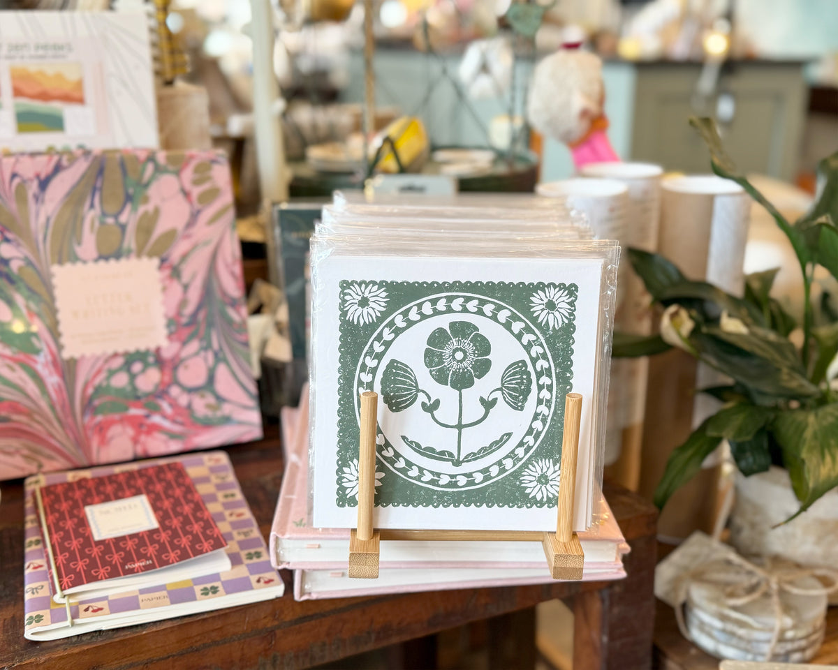 Stack of greeting cards with a floral design on a wooden table in a store setting.