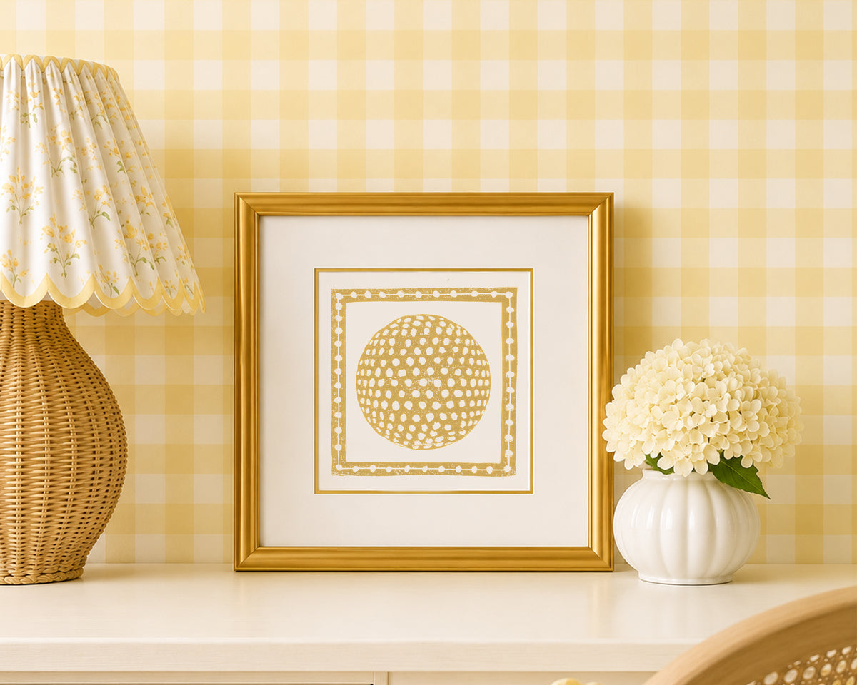 A mustard yellow and white golf ball art print in a gold matted frame on a styled shelf in a yellow and white bedroom