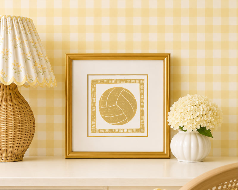 A mustard yellow and white volleyball art print in a gold matted frame on a styled shelf in a yellow and white bedroom
