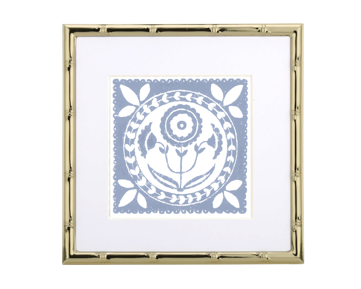 Framed artwork with a white floral design on a light blue background, inside a gold frame.