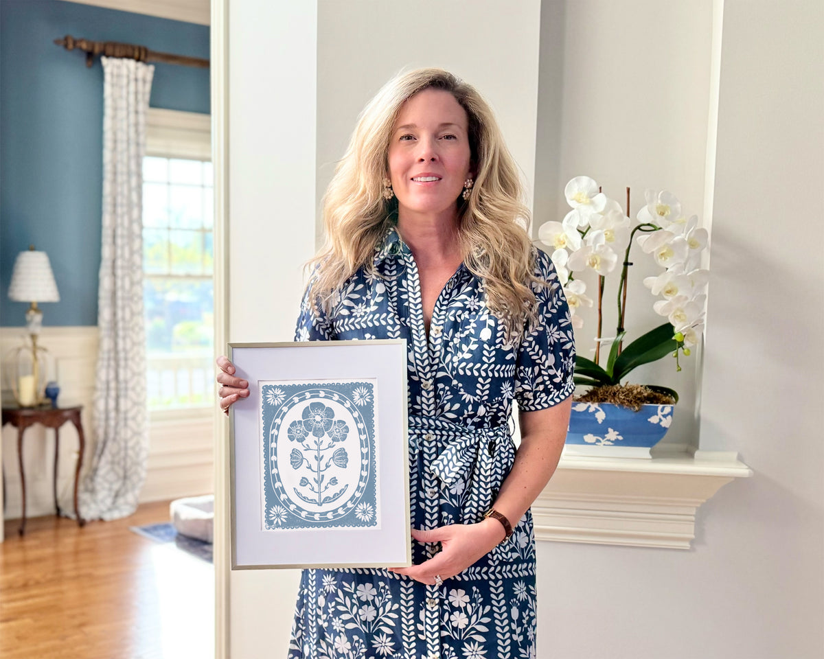 Woman holding a framed artwork in a home setting with decor elements.