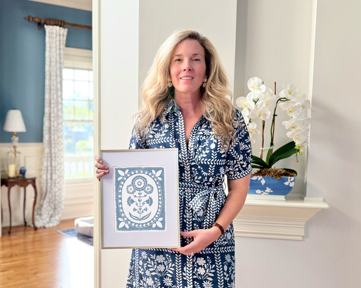 Woman holding a framed artwork in a home setting with decor elements.