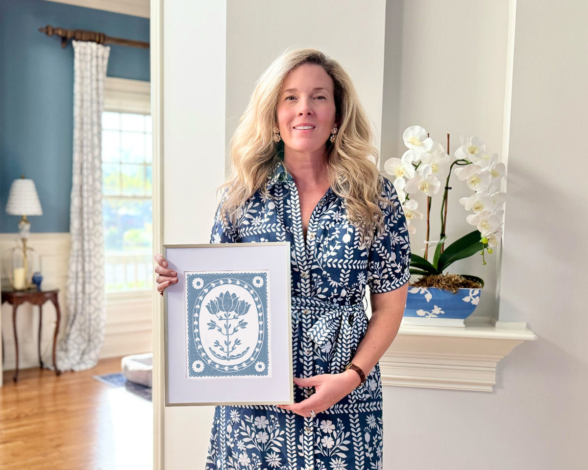 Woman holding a framed artwork in a home setting with decor elements.