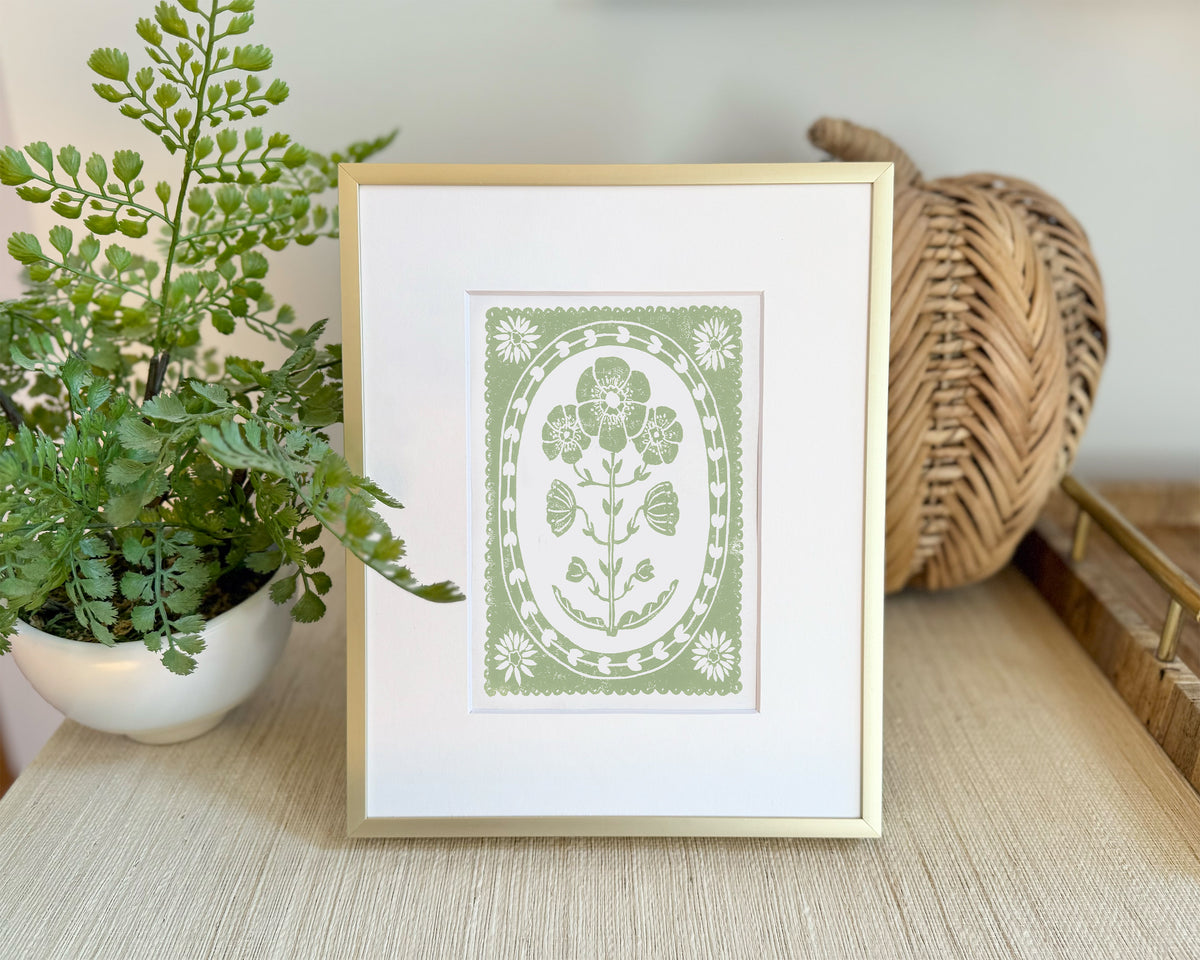 Framed artwork with floral design on a table next to a plant